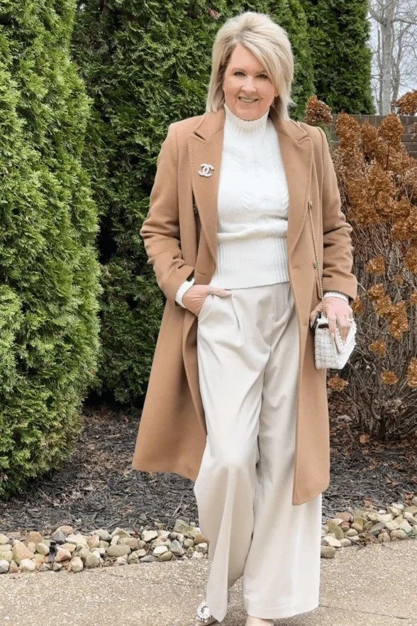 Winter outfit for women over 60: camel coat, white turtleneck, white wide pants