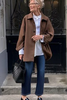 Winter outfit for women over 60: brown suede jacket, white top, blue jeans, loafers, doorway