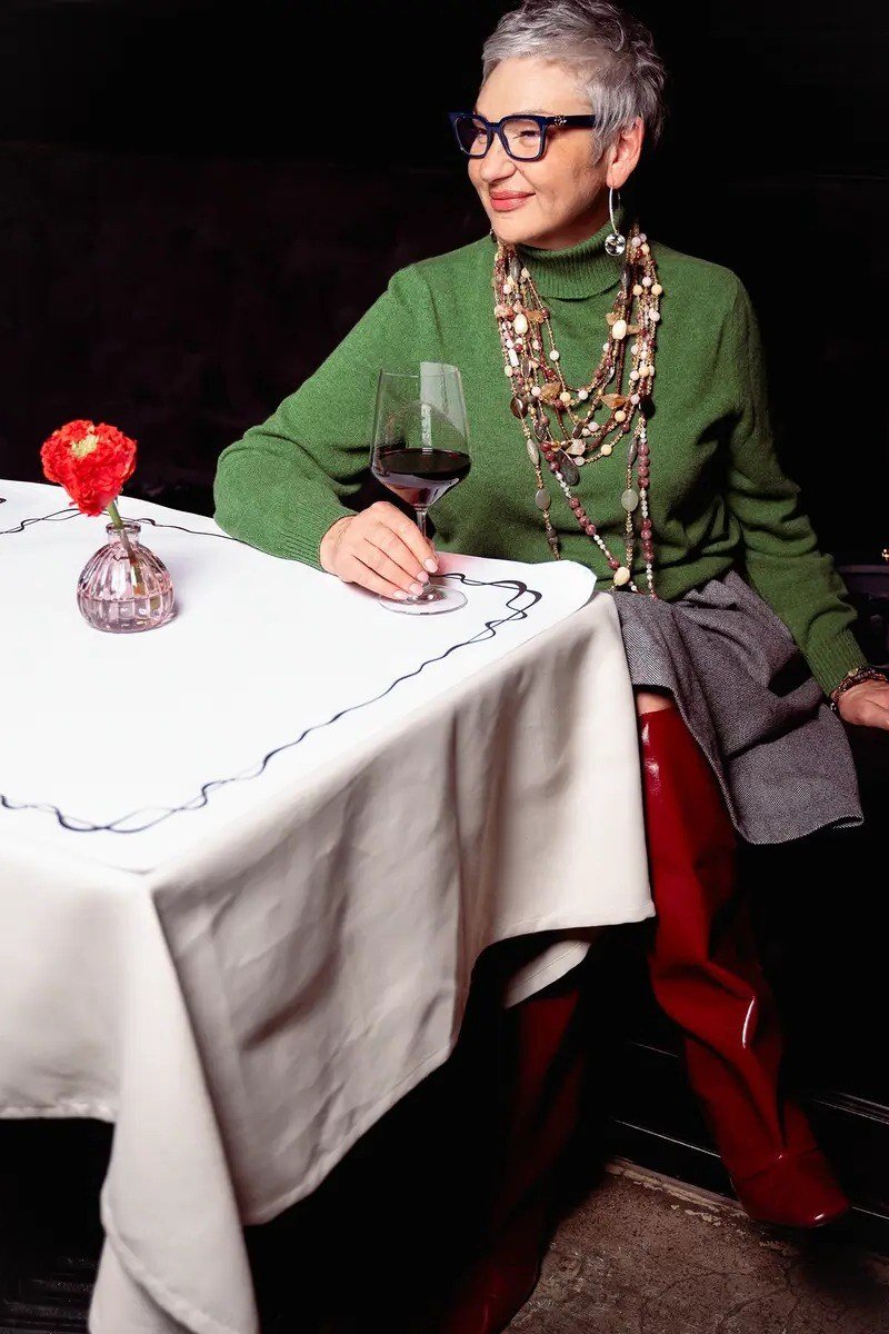winter date night outfit for women over 60: green knit sweater with red pants and layered necklaces at the dinner table