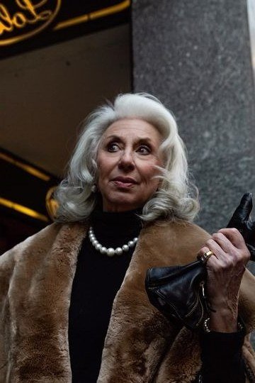 winter date night outfit for women over 60: fur-trimmed coat with pearl necklace on a night street