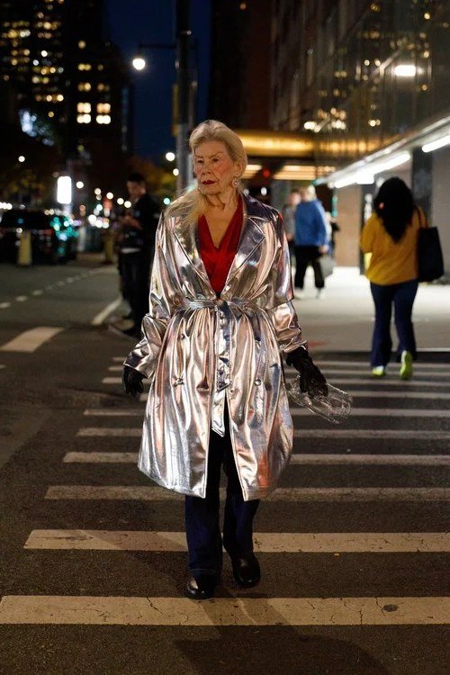 winter date night outfit for women over 60: silver metallic coat over a red dress on a night crosswalk