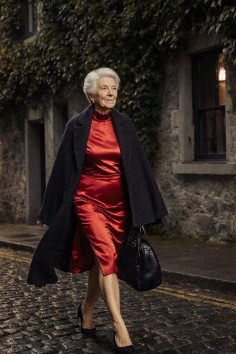 winter date night outfit for women over 60: red satin dress with a black coat on a cobblestone night street