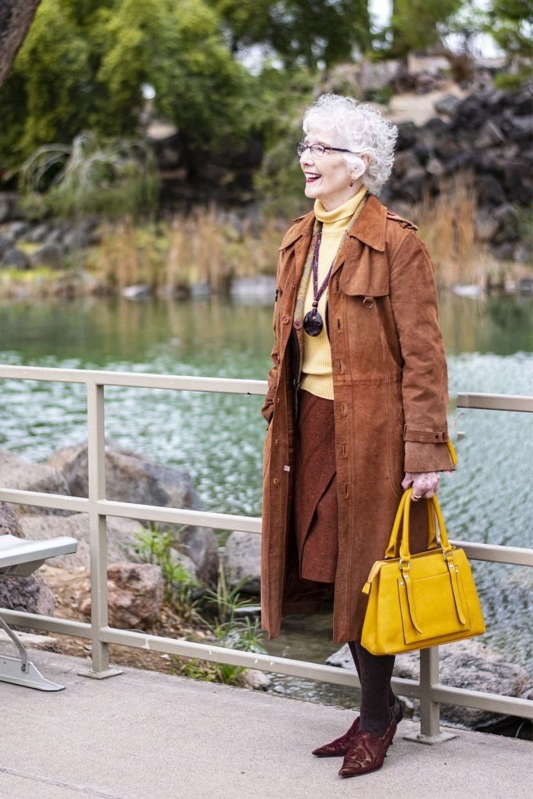 winter date night outfit for women over 60: tan leather coat with a rust skirt and yellow bag in a park