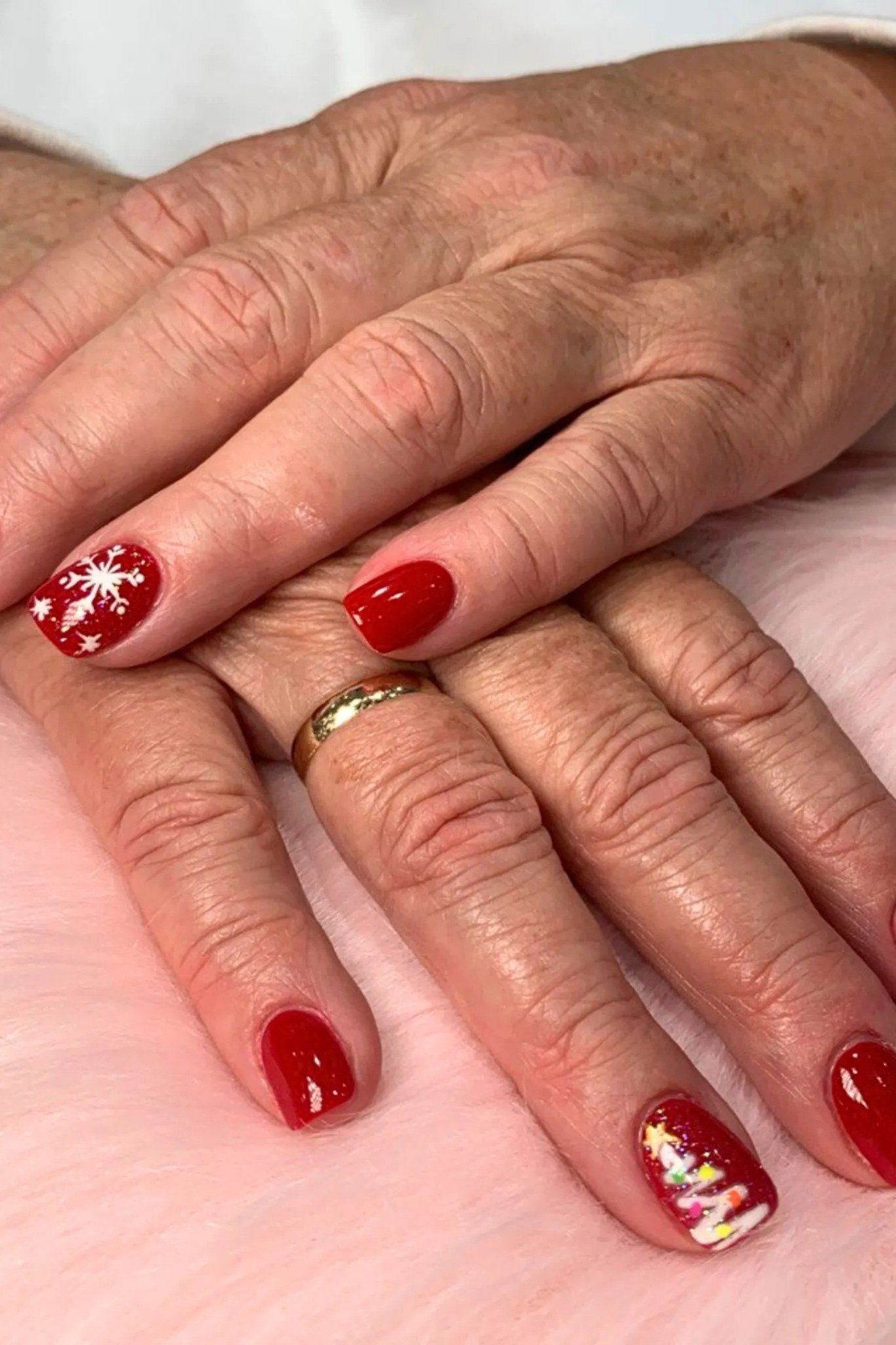 Red nails with gold glitter and snowflake accents on mature hands