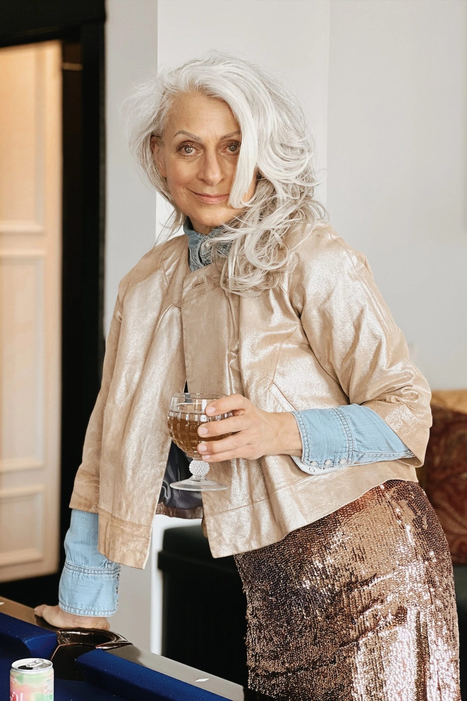 Woman in champagne satin blouse with bronze sequin skirt holding wine glass, warm metallic New Year's Eve outfit for women over 60