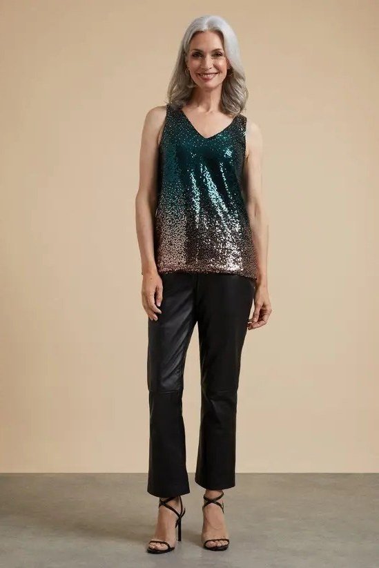 Gray-haired woman in teal sequin tank top with black pants, jewel-toned New Year's Eve outfit for women over 60
