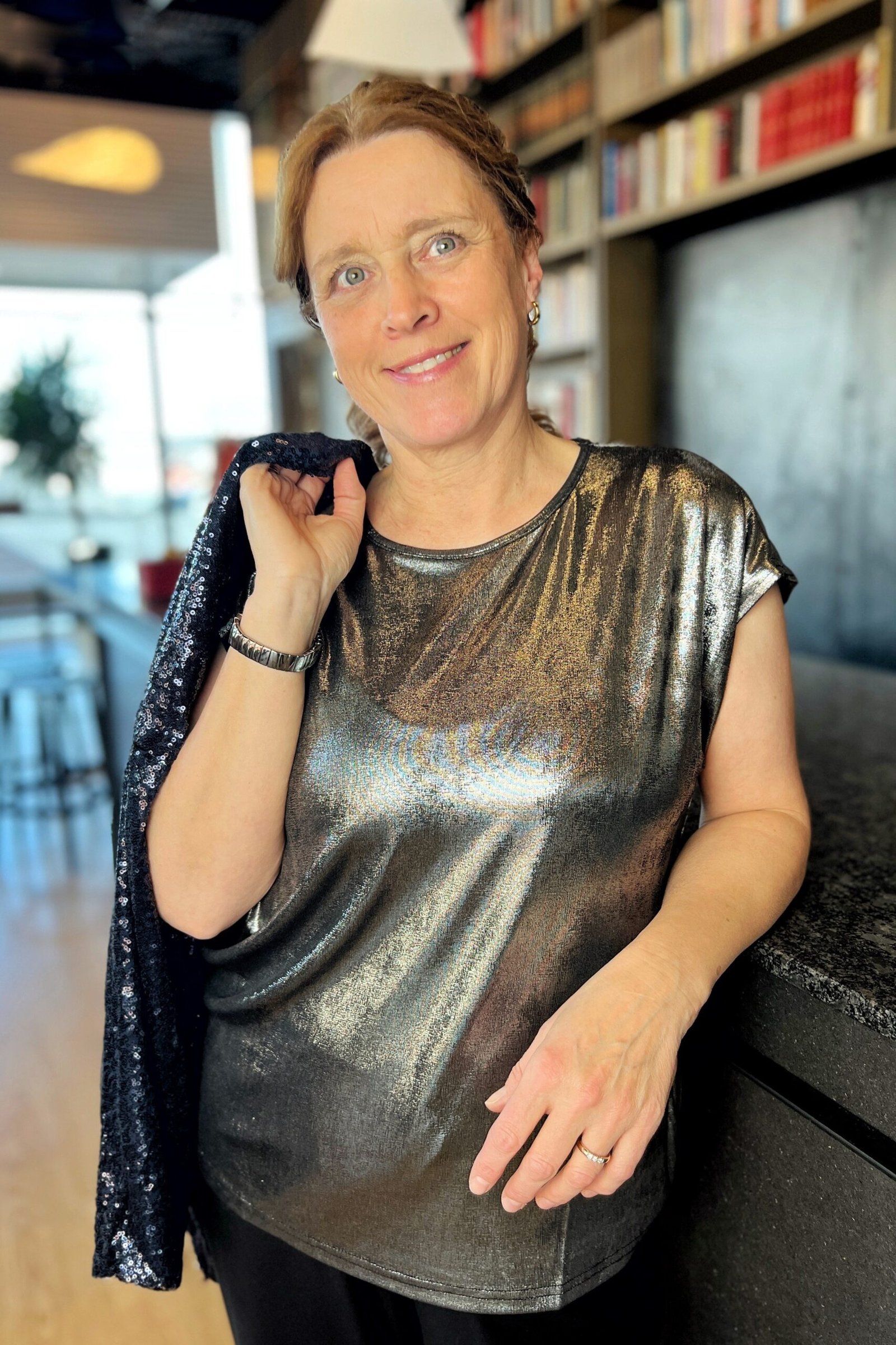 Woman in metallic silver top with dark sequin jacket draped over shoulder, layered New Year's Eve outfit for women over 60