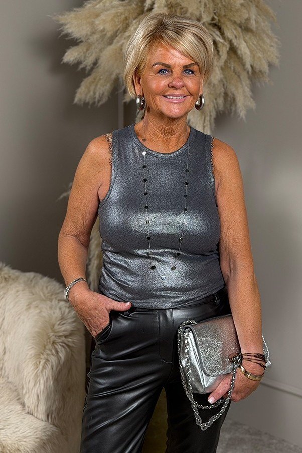 Blonde woman in silver metallic tank top with leather pants and silver clutch, modern New Year's Eve outfit for women over 60