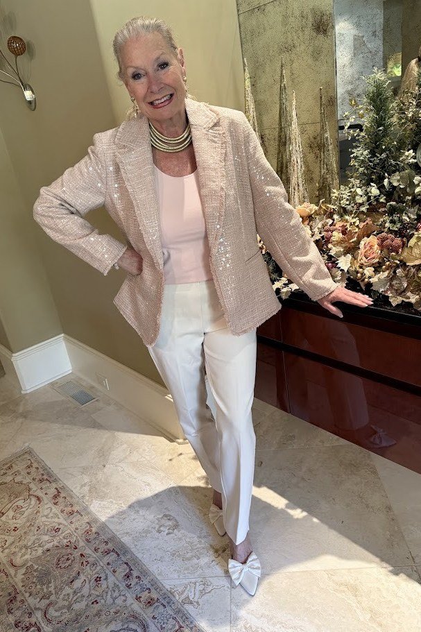 Woman in champagne sequin blazer with white pants in marble hallway, luxurious New Year's Eve blazer outfit for women over 60