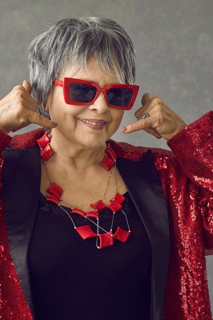 Gray-haired woman in red sequin blazer with red statement necklace and red sunglasses, head-to-toe red New Year's Eve blazer outfit for women over 60