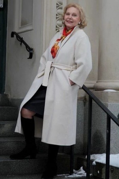 Cream belted coat over black skirt with red patterned scarf and knee boots, classic winter outfit for women over 60