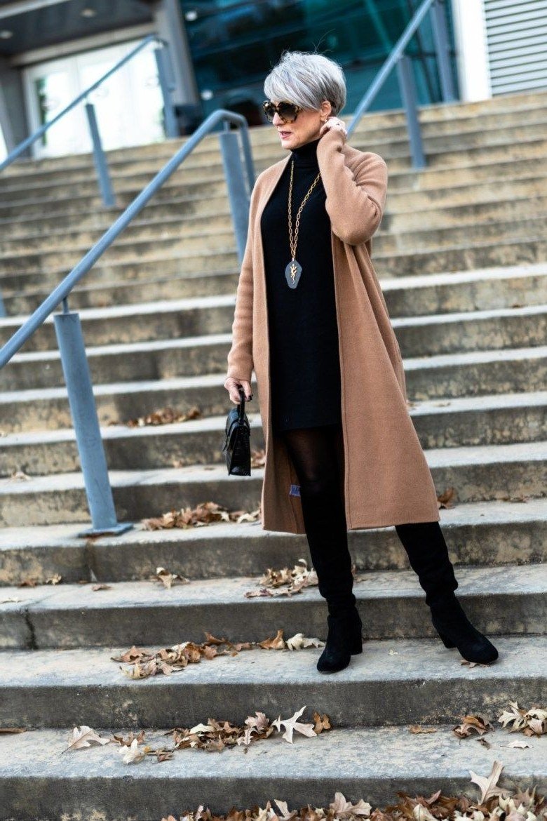 Warm tan coat over black turtleneck and black trousers with knee boots, sharp winter layering look for women over 60