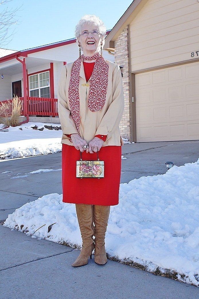 Cream coat over red patterned scarf and bright red midi skirt with tan boots, cheerful winter outfit for older women