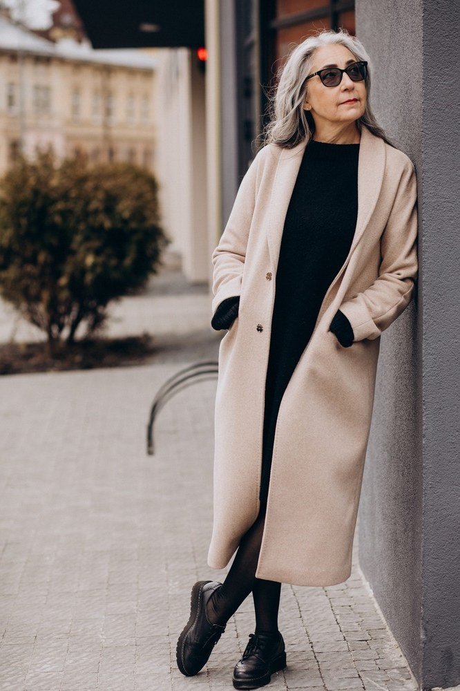 Soft beige coat over black turtleneck and black trousers with ankle boots, light and dark winter outfit for women over 60