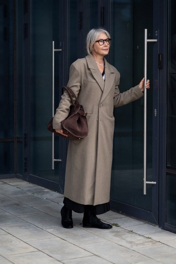 Long taupe coat over black trousers with brown leather bag, quiet luxury winter outfit for older women