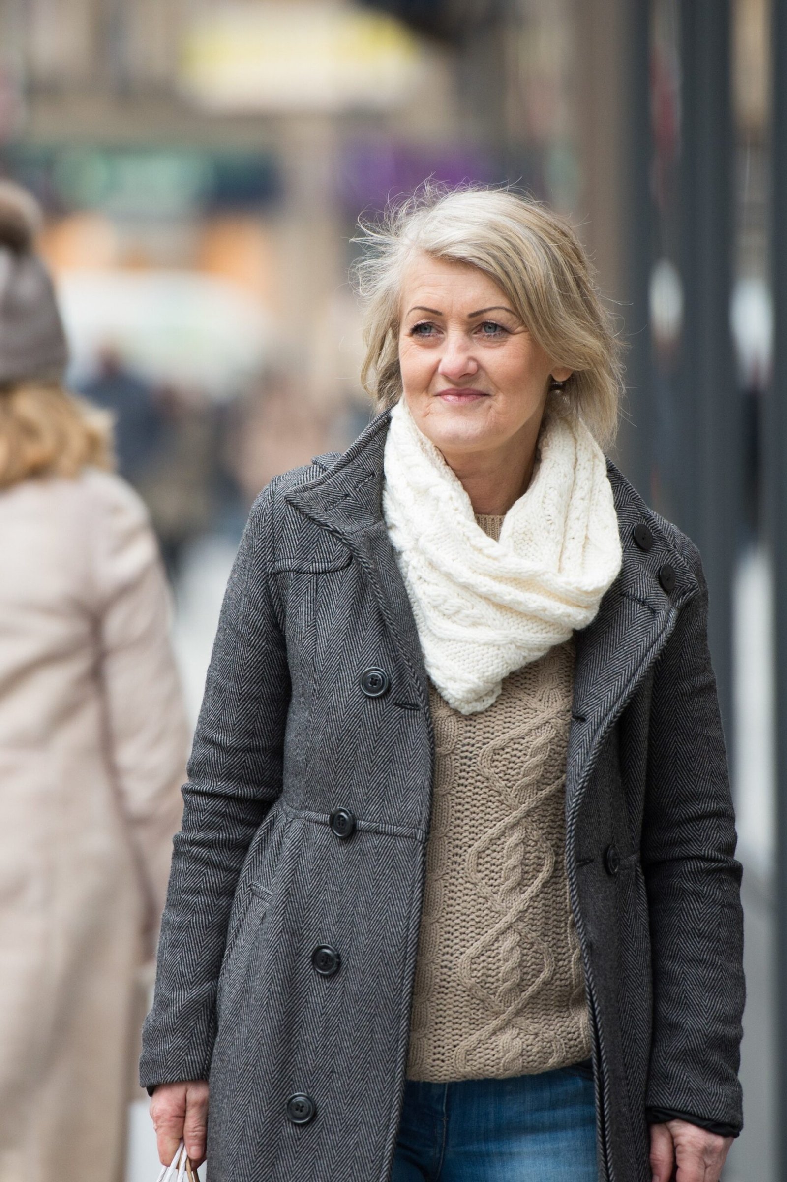 Gray buttoned coat over beige cable knit sweater with white chunky scarf and jeans, cozy winter outfit for women over 60