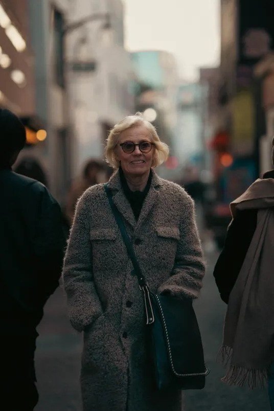 Gray tweed coat over beige sweater with white scarf and blue jeans, heritage winter street style for women over 60