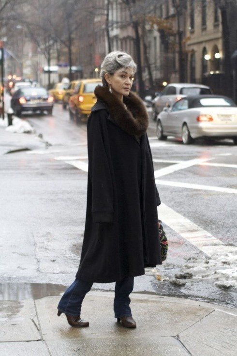 Black long coat with brown fur collar over blue jeans and brown boots, glamorous winter layering outfit for older women