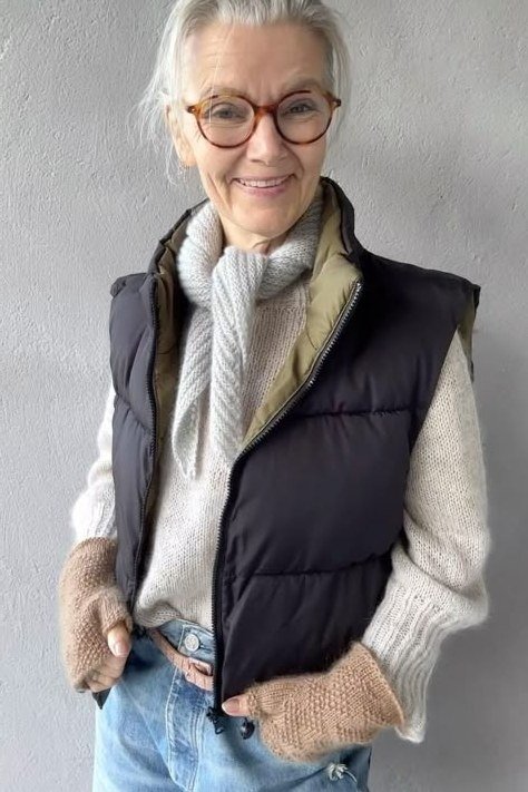 Black quilted puffer vest over cream cable knit sweater and blue jeans, casual weekend winter layering outfit for women over 60
