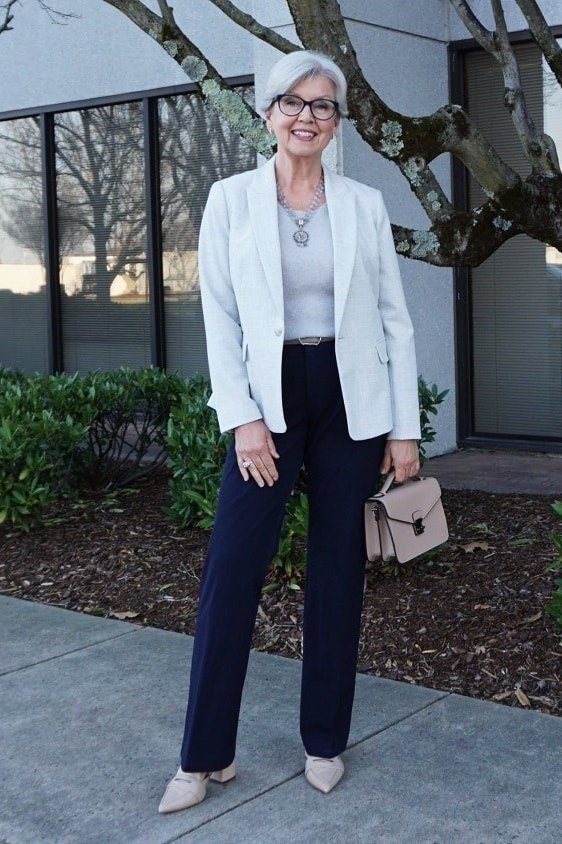 Older woman in white blazer and navy trousers holding a pink clutch on a city street