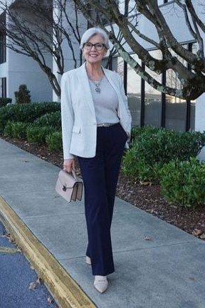 Older woman in light gray blazer, white top and navy trousers on a sidewalk