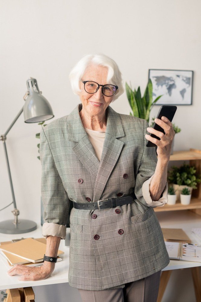 Older woman in gray plaid double-breasted blazer holding a phone in an office