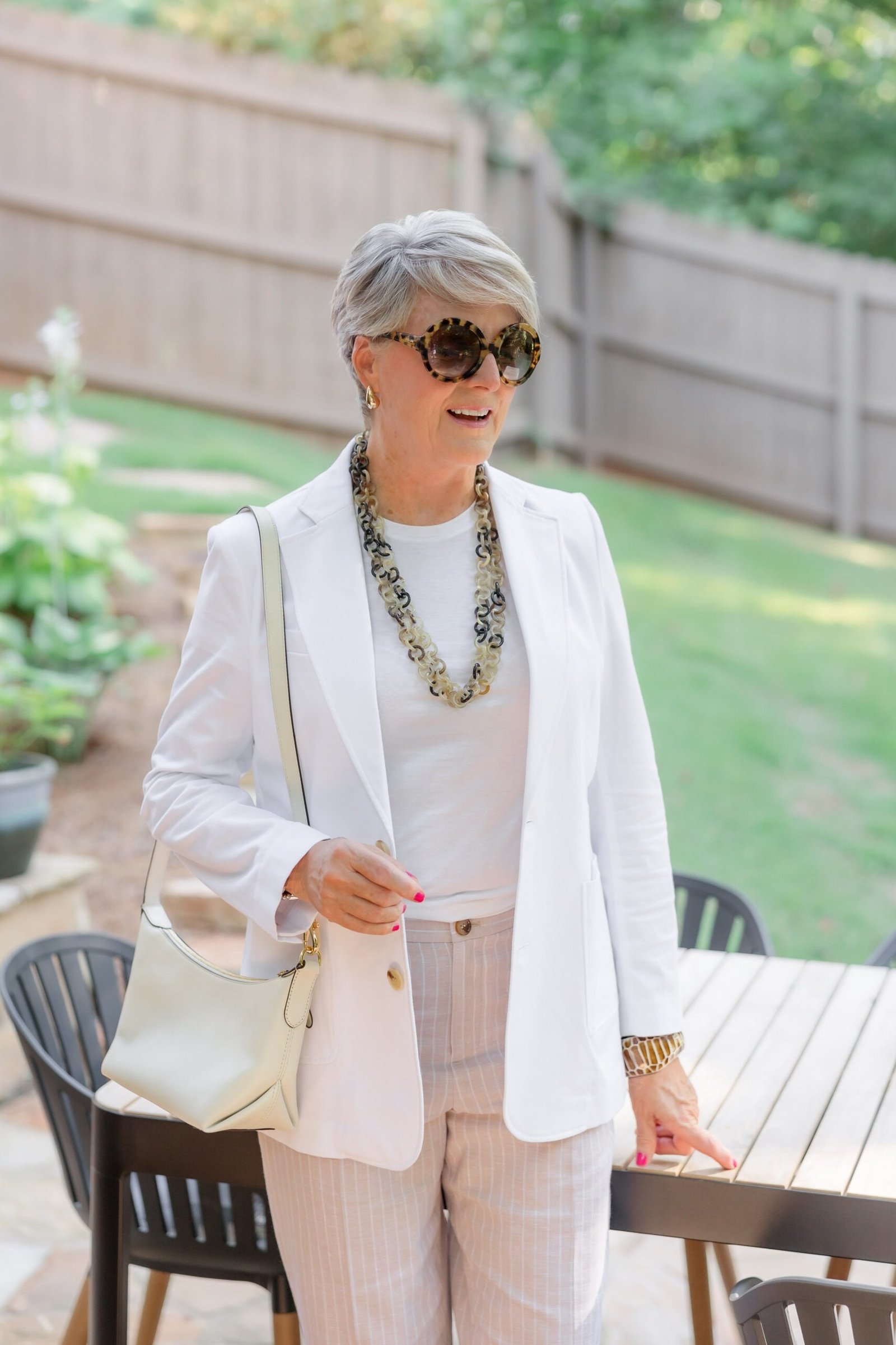 Older woman in white blazer and pink striped trousers in a backyard