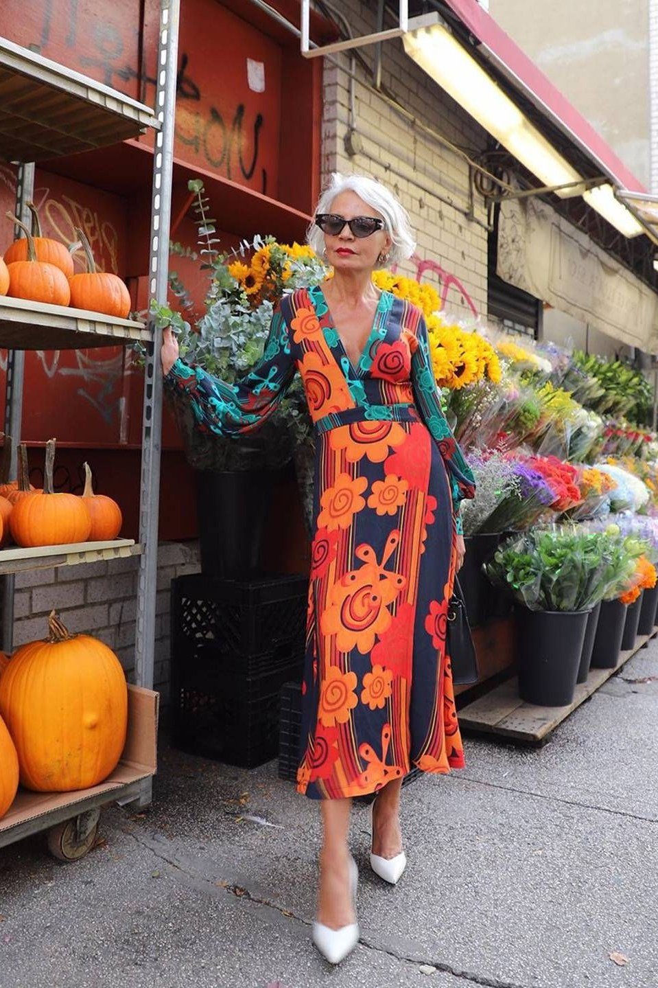Gray-haired woman over 60 in an orange floral wrap midi dress with sunglasses on a market street
