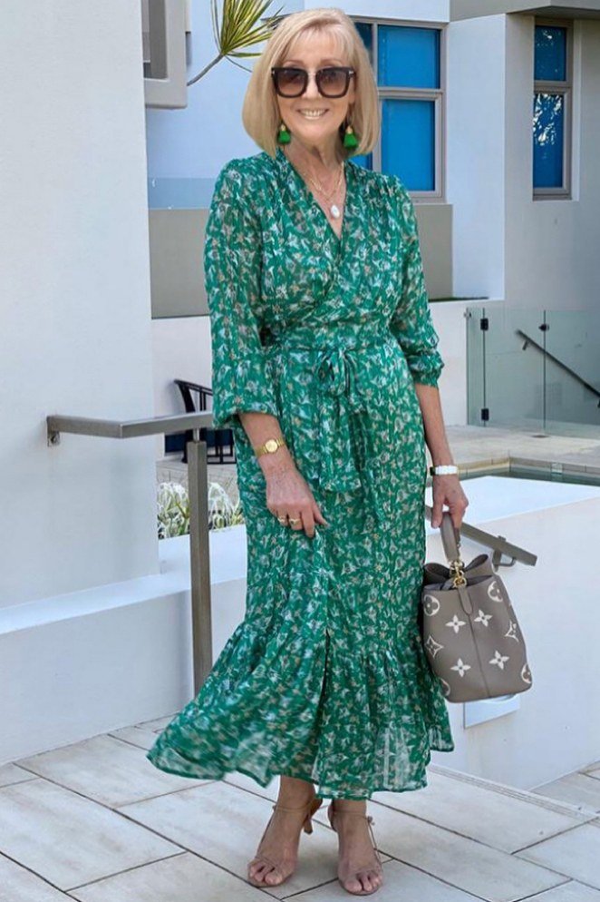 Blonde woman over 60 wearing a green floral wrap maxi dress with tie belt on a patio