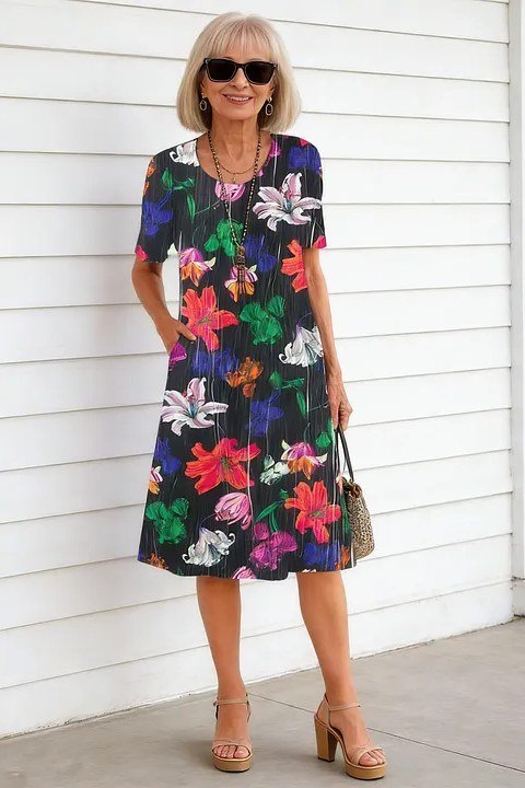 Blonde woman over 60 wearing a dark floral wrap midi dress with sunglasses