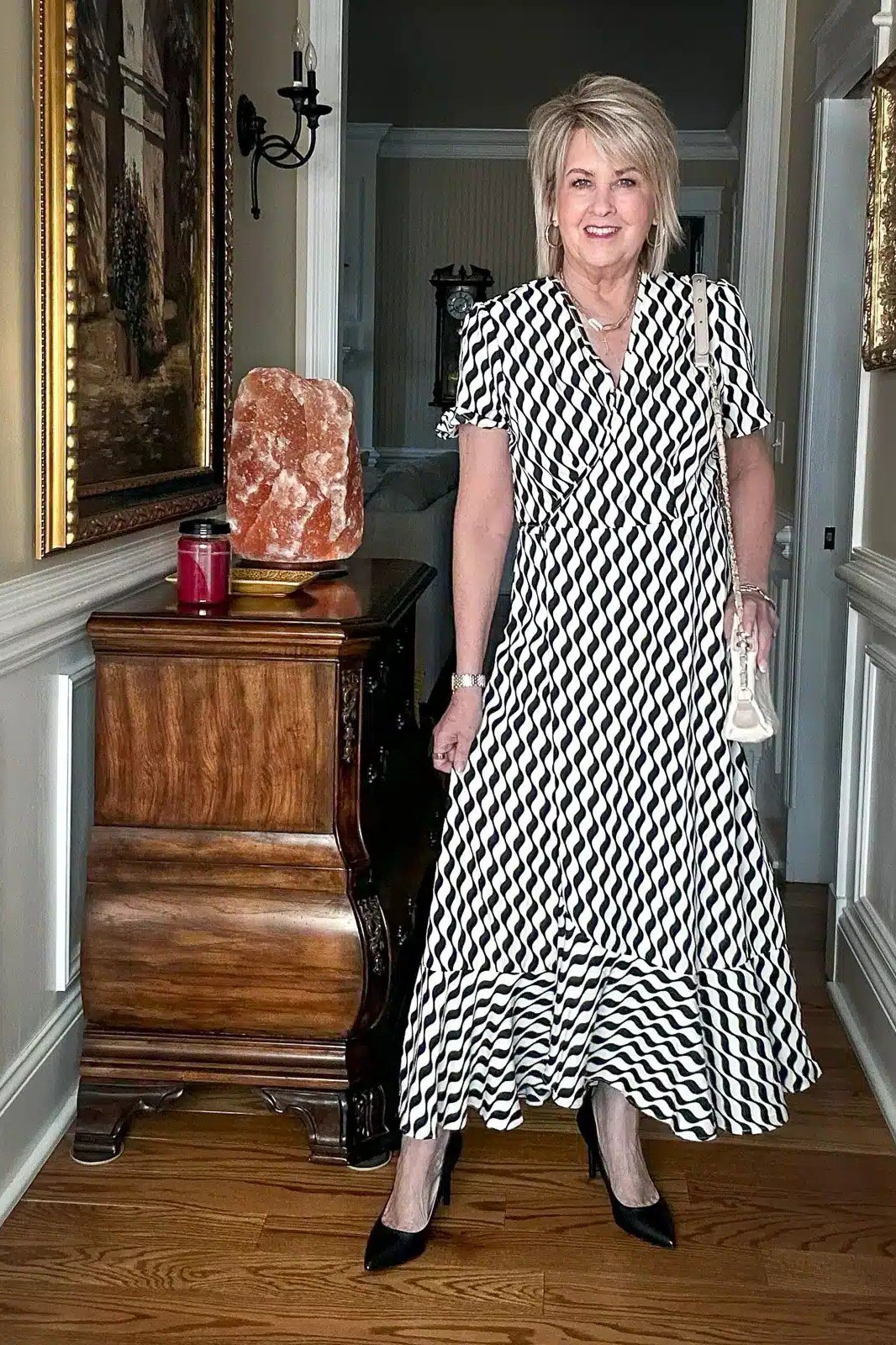 Blonde woman over 60 in a black and white chevron wrap maxi dress in a doorway
