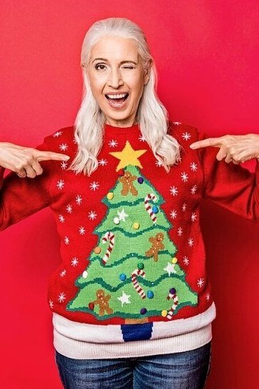 Red Christmas Tree Sweater with Jeans worn by older woman, red Christmas tree sweater with jeans on red backdrop
