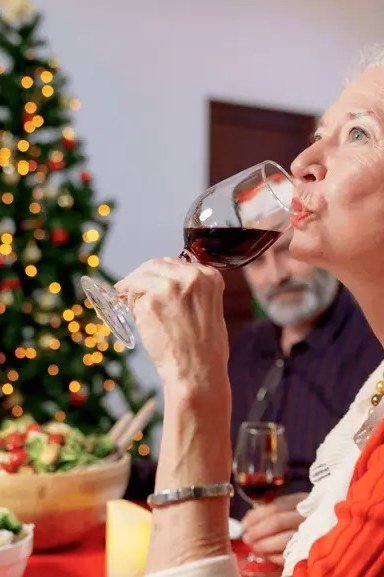 Santa Hat and a Glass of Red Wine worn by older woman, santa hat and red top drinking wine at Christmas dinner