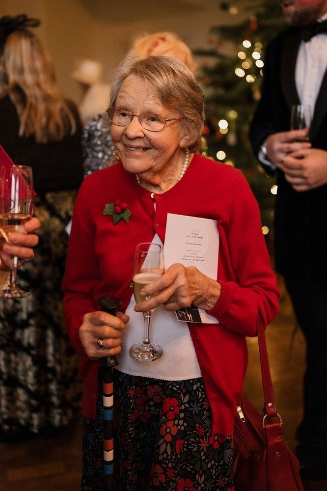 Red Cardigan with a Brooch at the Party worn by older woman, red cardigan with brooch holding champagne at party