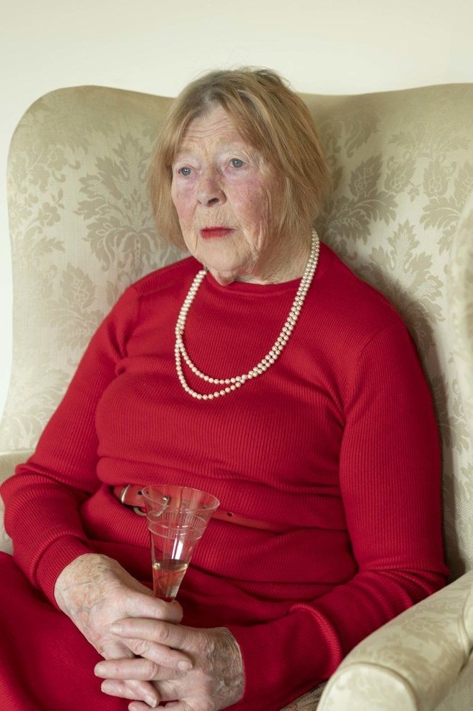Red Dress with Pearls and Champagne worn by older woman, red dress with pearls holding champagne seated