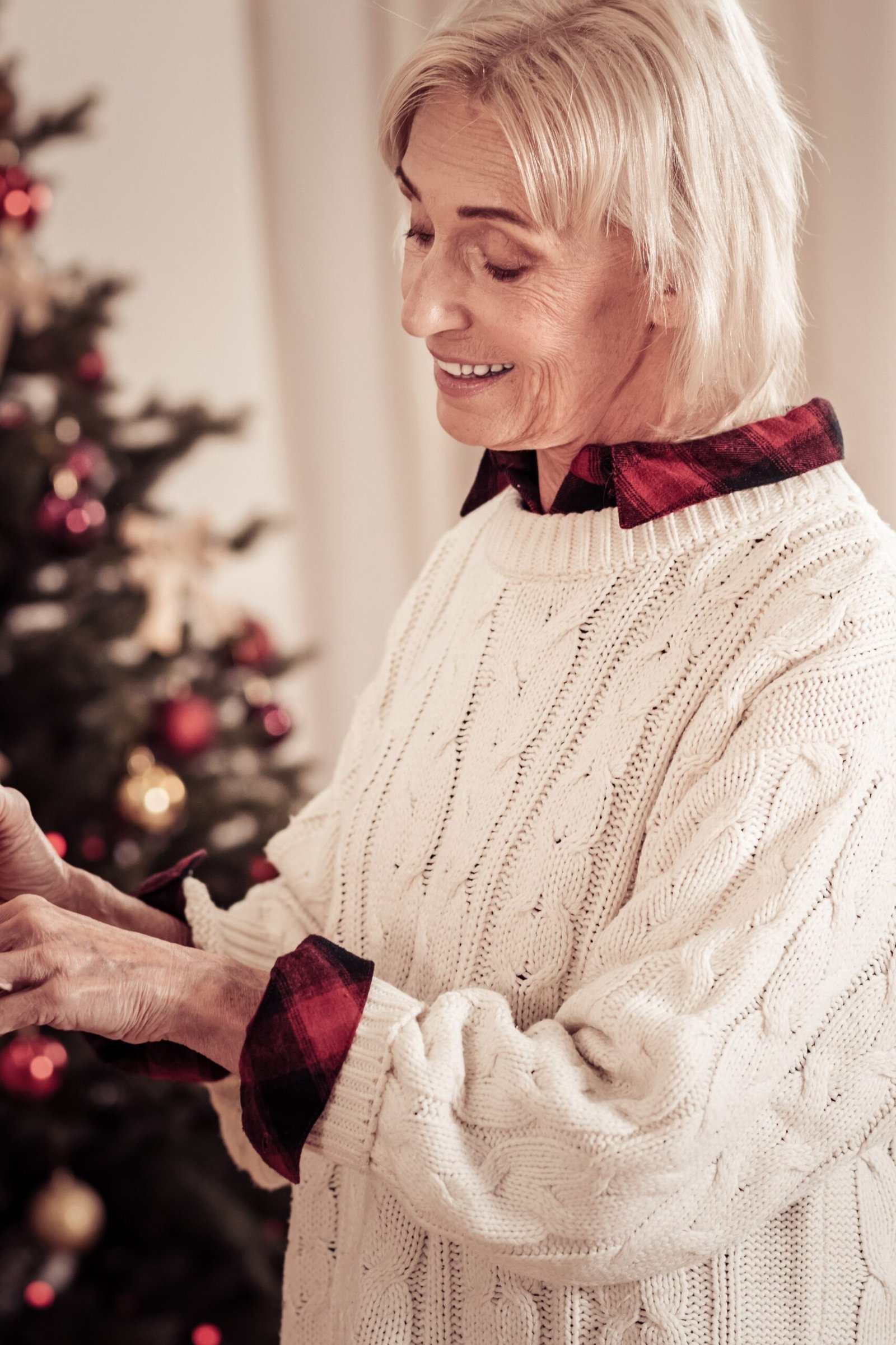 Cream Cable-Knit Sweater Wrapping a Gift worn by older woman, cream cable-knit sweater wrapping gift by Christmas tree