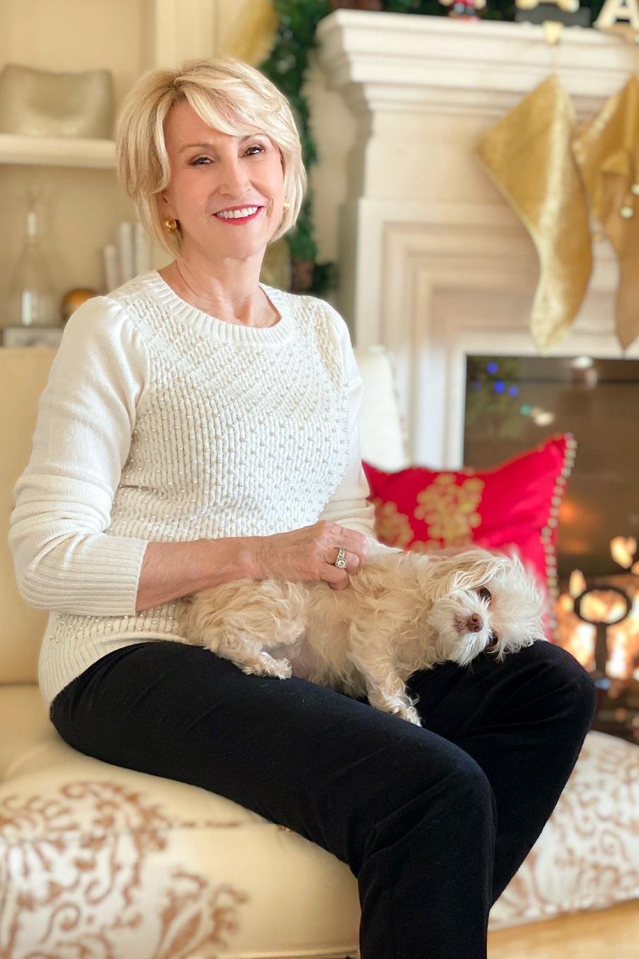 White cable knit Christmas sweater with black pants by fireplace, cozy holiday outfit for women over 70