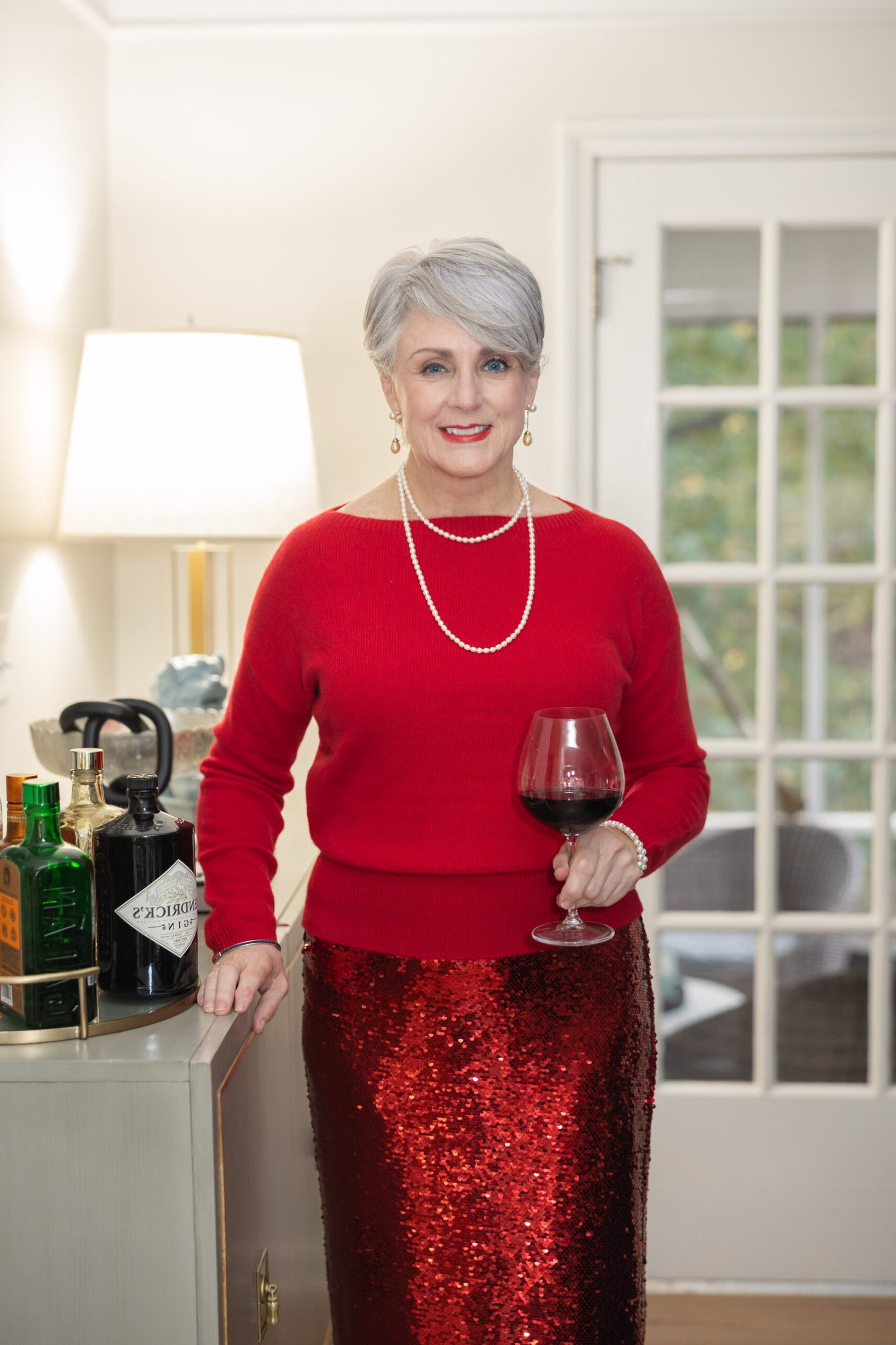 Red top with red sequin midi skirt holding wine glass, Christmas party outfit for women over 70