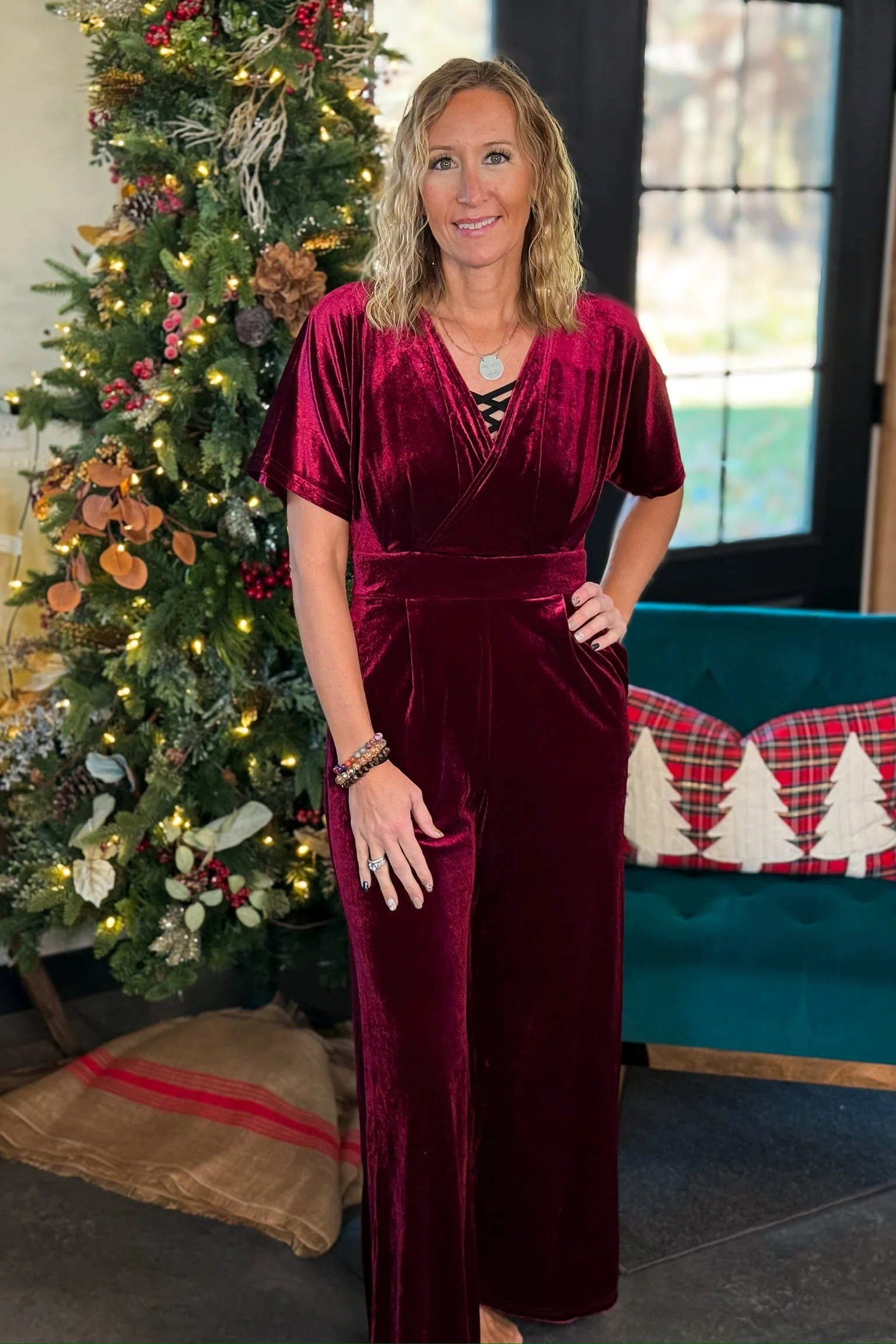 Burgundy velvet jumpsuit with waist tie by Christmas tree, elegant holiday outfit for women over 70